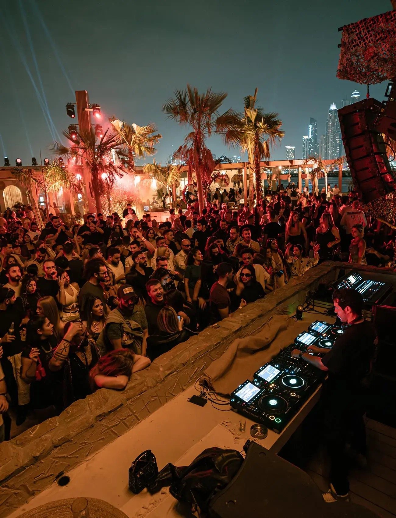 The open-air Be Beach crowd among the palms, Dubai Marina skyline behind